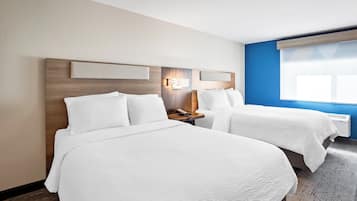 A hotel room with two beds, a nightstand with a lamp, and a window with blinds.