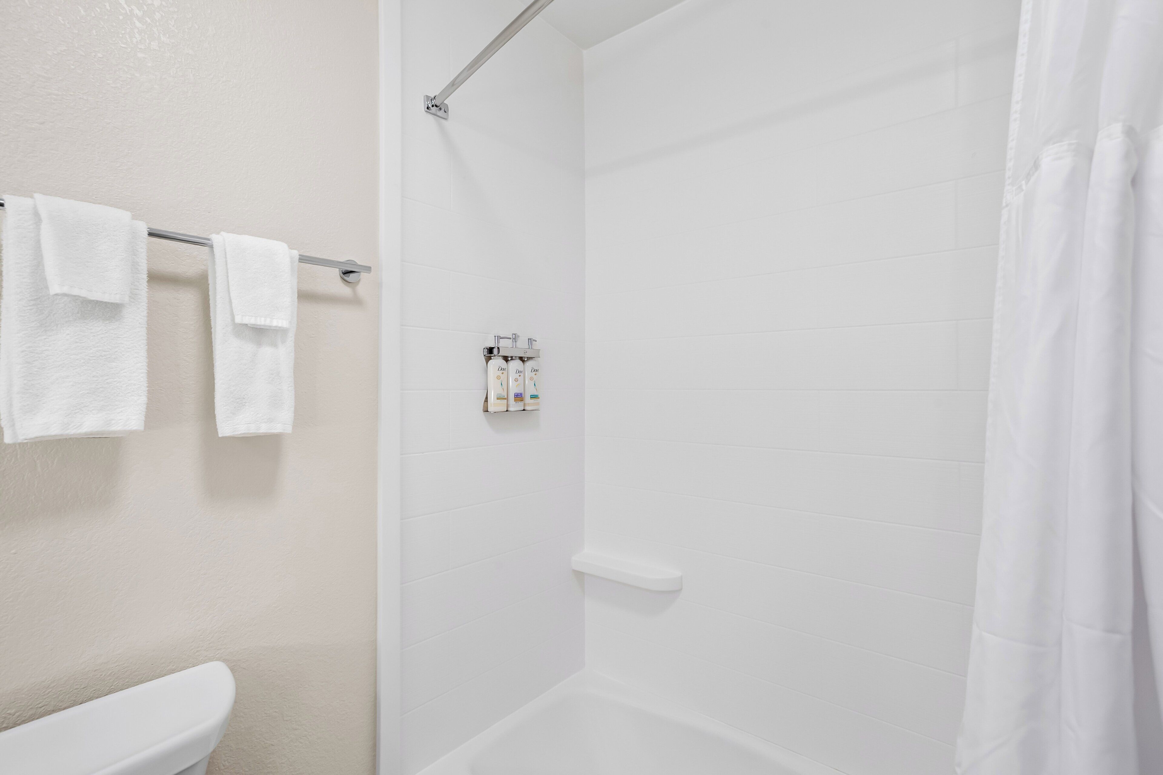 A bathroom with a toilet, a towel rack with two towels, a shower curtain, and a soap dispenser on the wall.