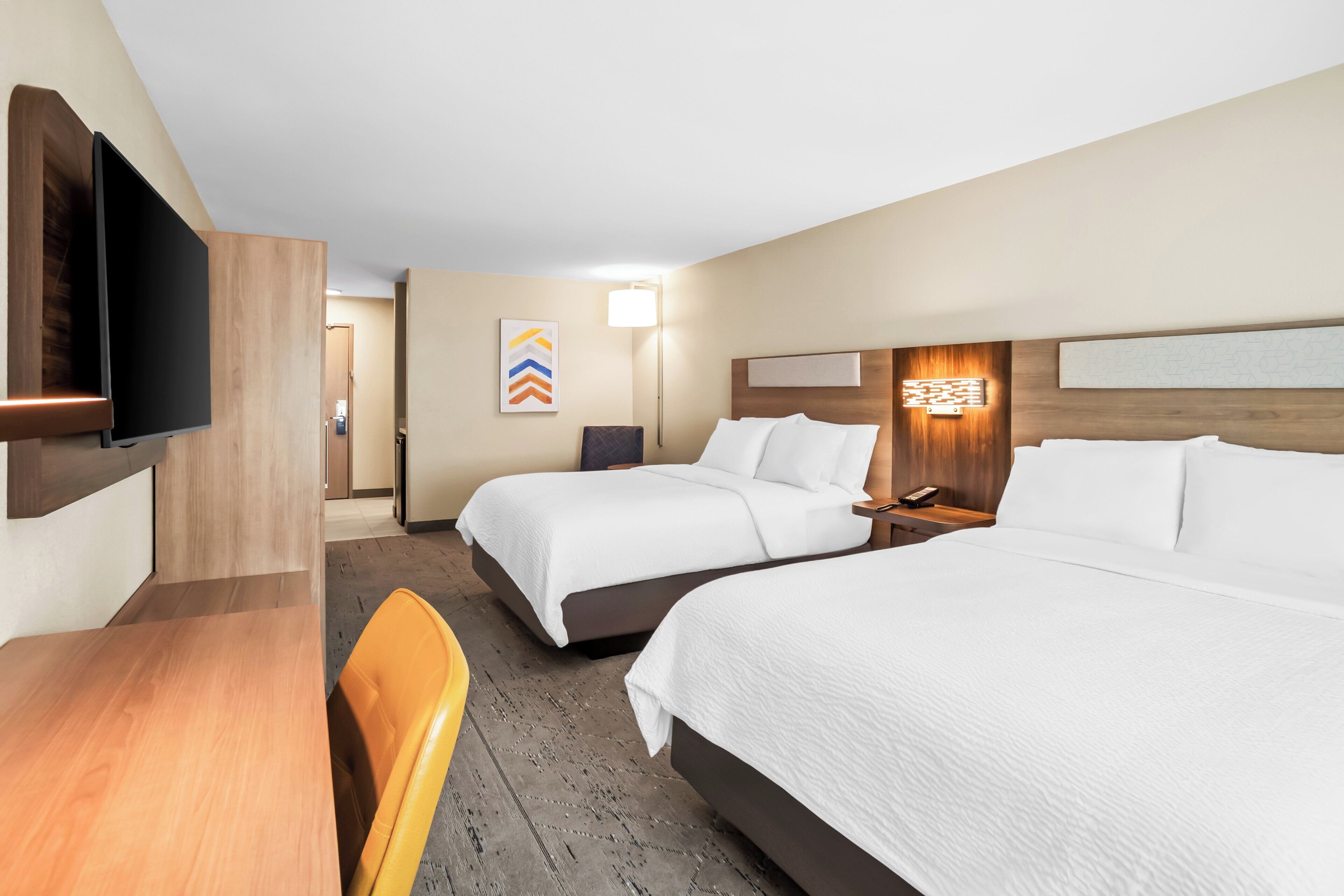 A hotel room with two beds, a desk, a chair, a TV, and a wall-mounted artwork.