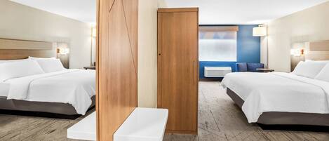 A hotel room with two beds, a small table, and a view of the city through the window.