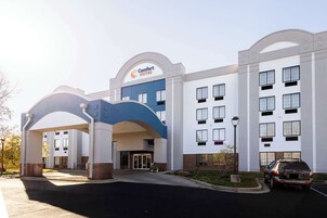 Un hotel Comfort Suites con diseño moderno, que cuenta con una entrada destacada con arco azul, varias ventanas y un área de estacionamiento.