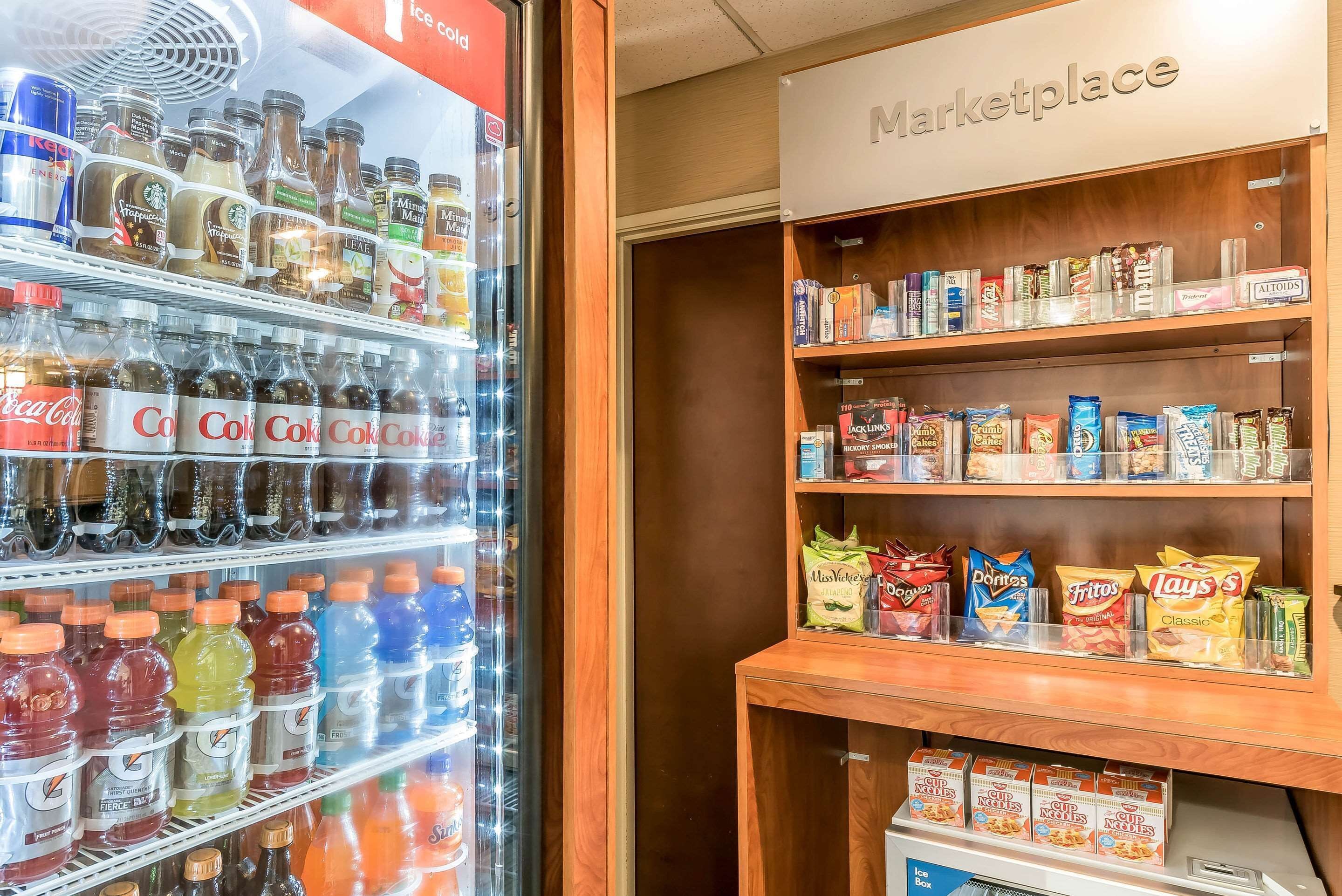 Un refrigerador lleno de bebidas variadas y un estante con papas fritas y galletas.
