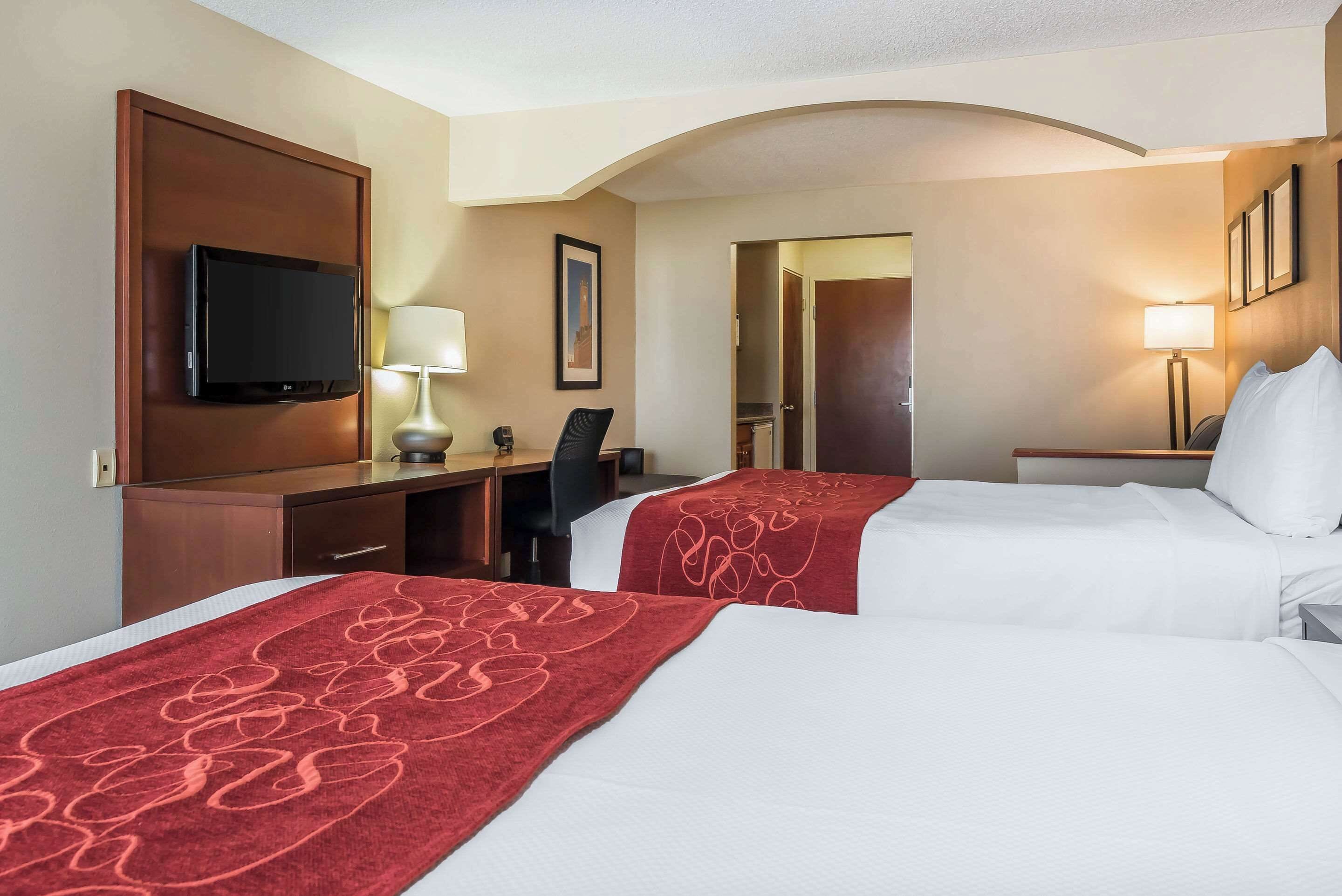 A hotel room with two beds, a desk, a TV, and a door leading to a bathroom.
