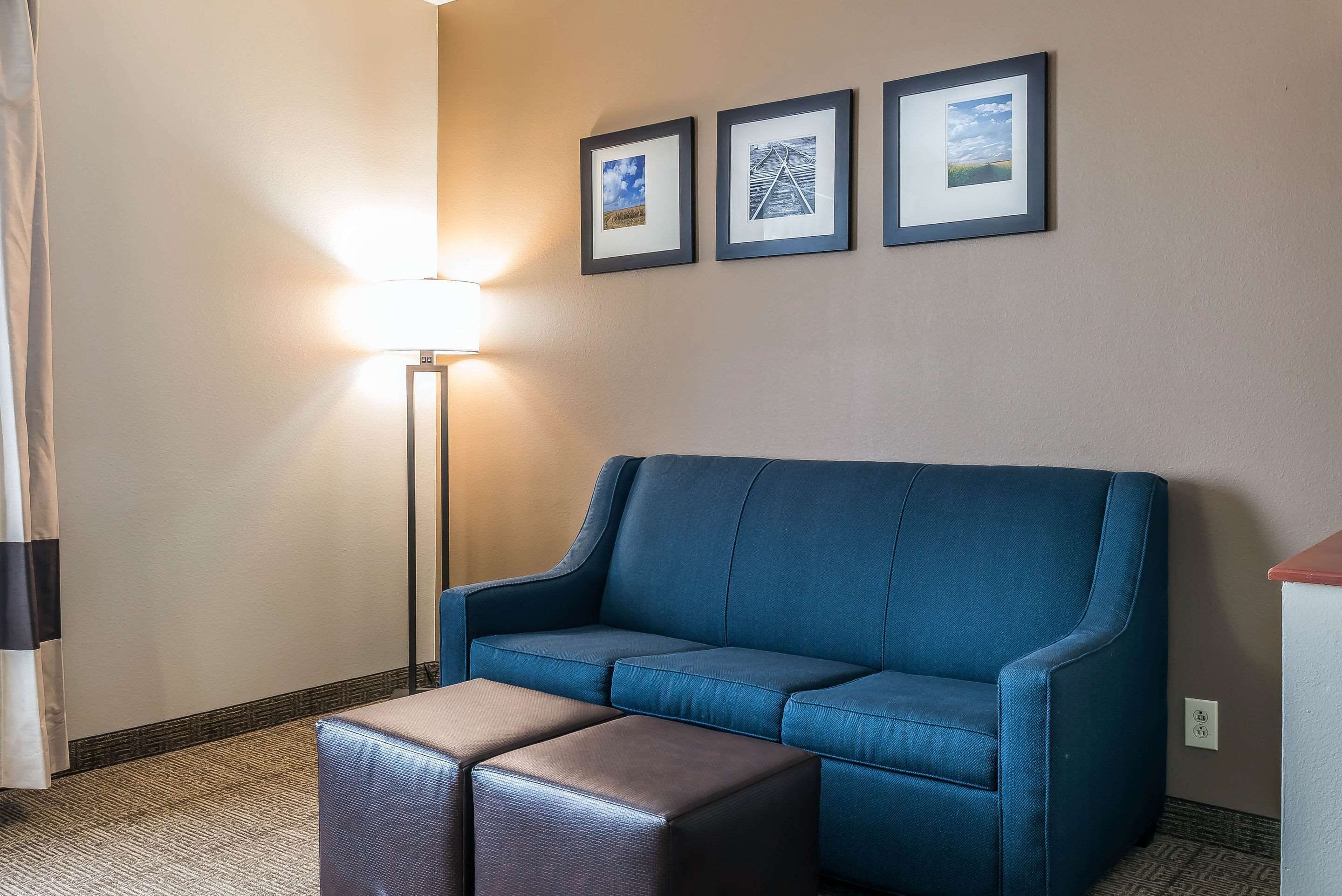 A blue sofa with a matching ottoman in a hotel room with a lamp and three framed pictures on the wall.