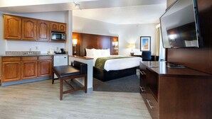 Habitación de hotel con cama, mesita de noche, escritorio, silla, kitchenette y televisor.