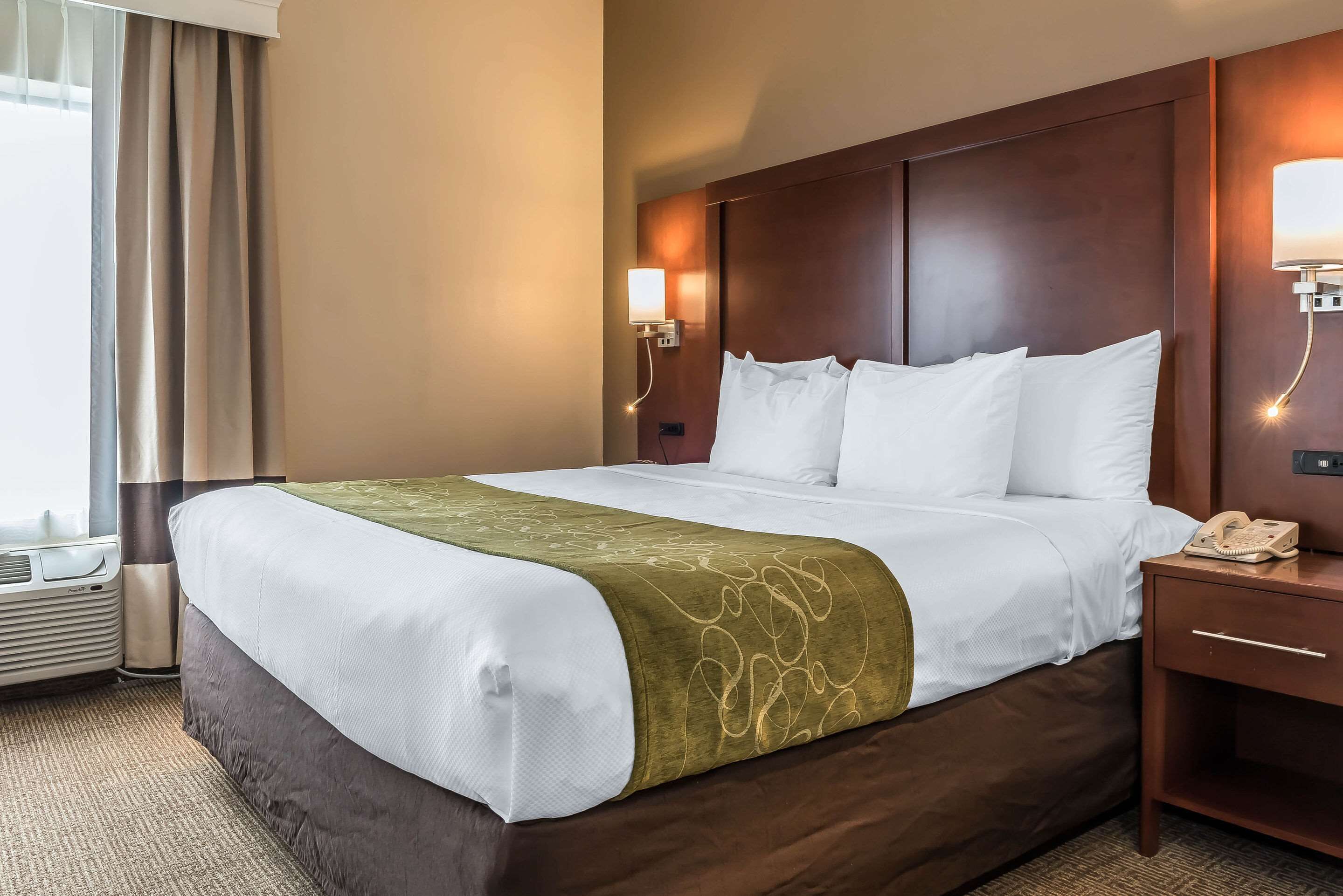 A hotel room with a large bed, a bedside table with a lamp, and a telephone.