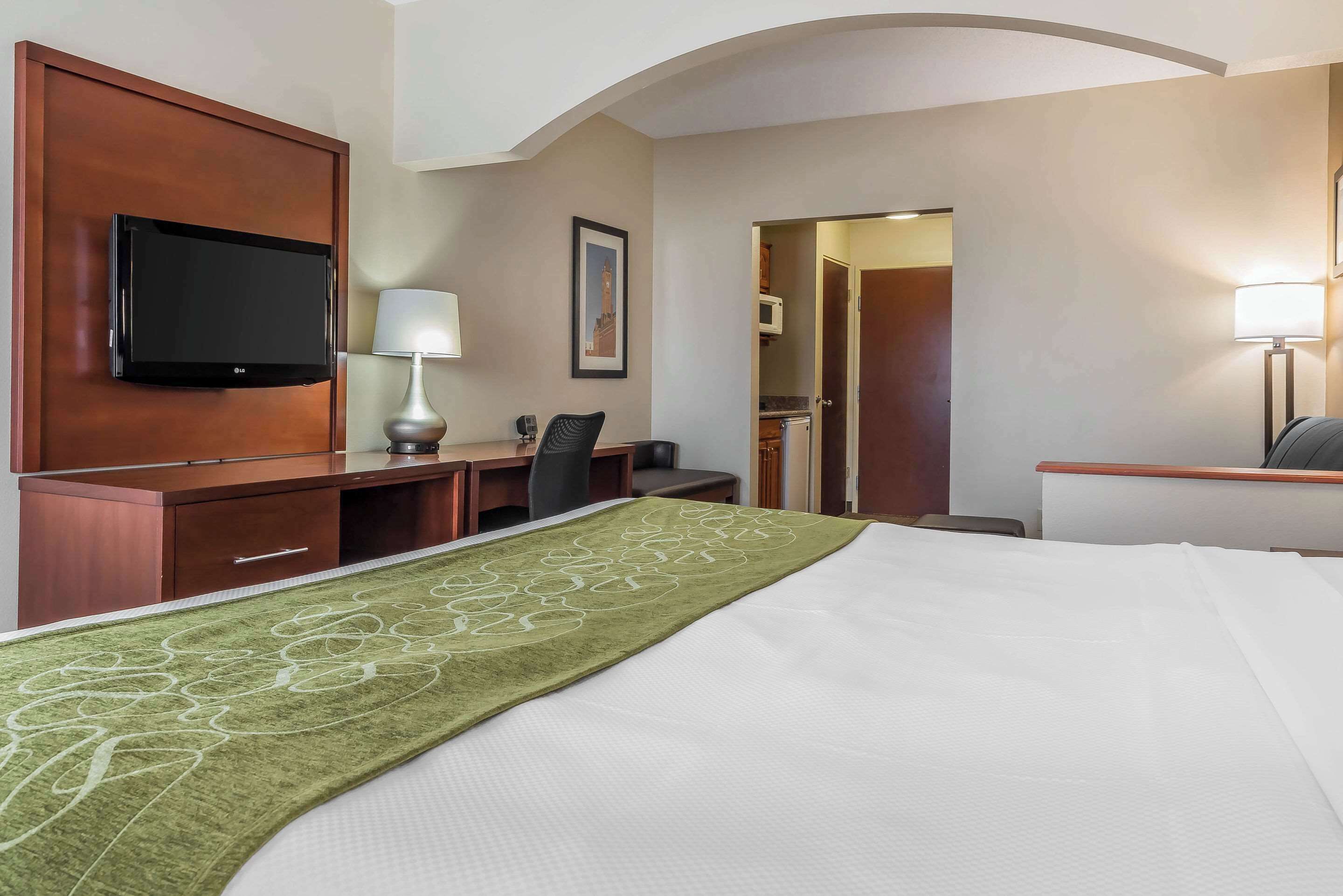 A hotel room with a bed, a desk, a chair, a TV mounted on the wall, and a door leading to a bathroom.