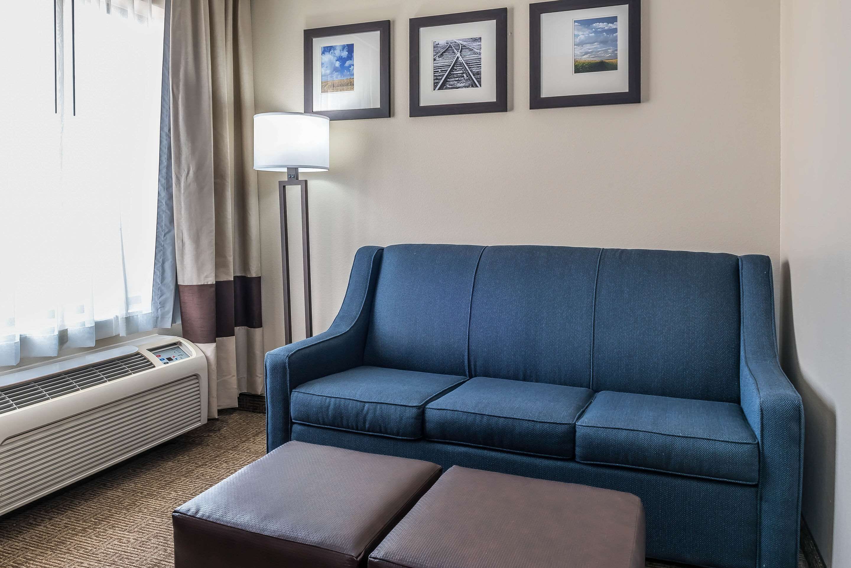 Un canapé bleu accompagné d’un pouf assorti, un lampadaire et trois tableaux encadrés accrochés au mur.