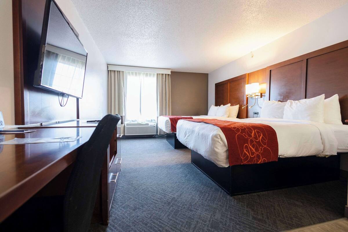 Une chambre d’hôtel équipée d’un bureau, de deux lits, d’une télévision et d’une fenêtre avec des rideaux.