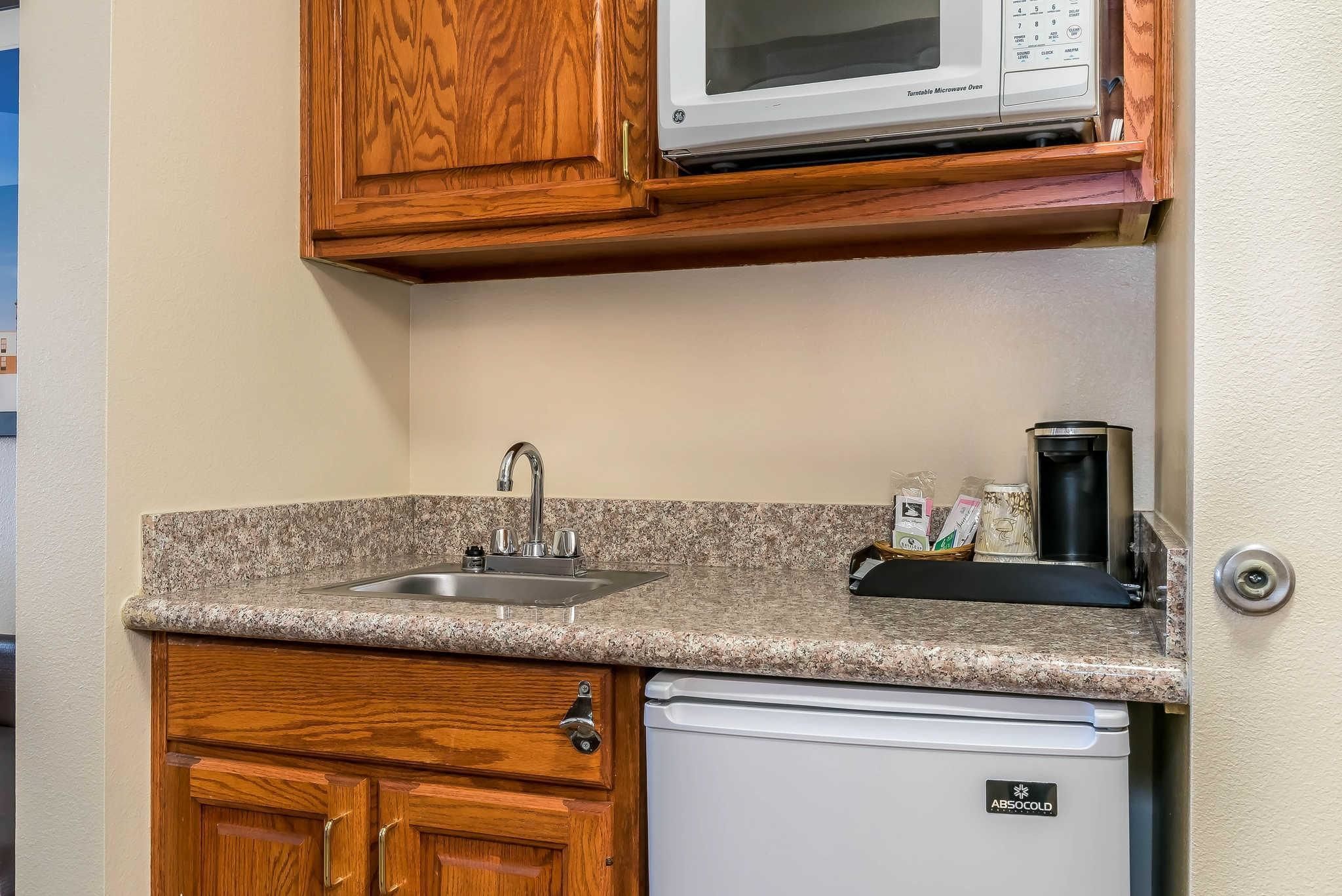 A compact kitchen with a granite countertop, a built-in microwave, a coffee maker, and a dishwasher.