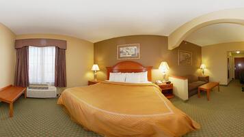 Quarto de hotel com uma cama grande, duas mesas de cabeceira com luminárias, uma cadeira, uma escrivaninha e um aparelho de ar condicionado.