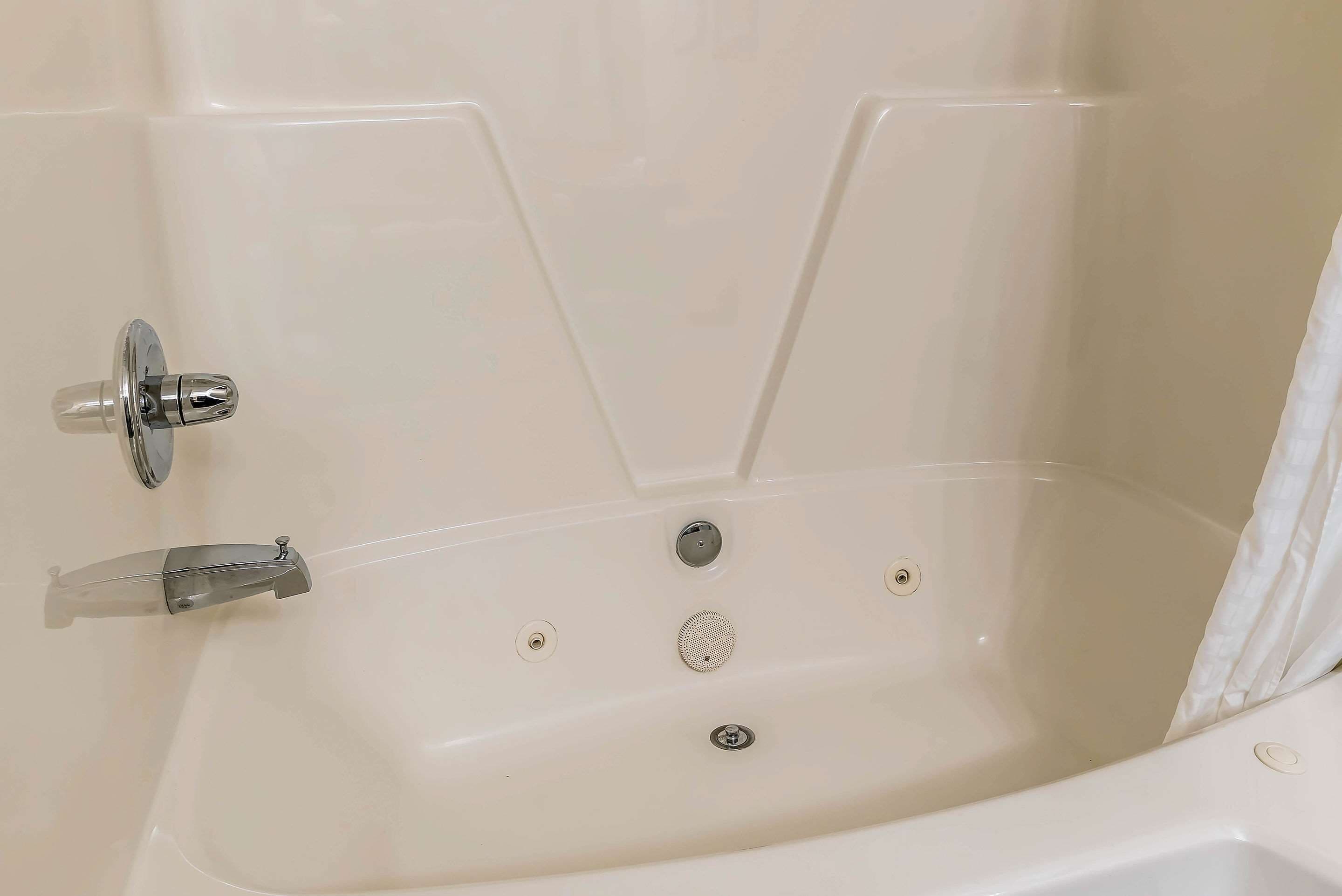Una bañera blanca con grifo de cromo y ducha, un panel de control con botones, y desagüe.