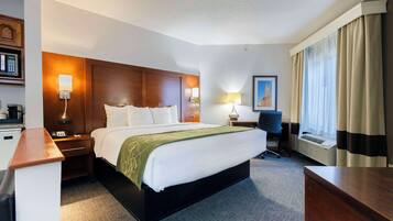A hotel room with a large bed, bedside tables, a desk, a chair, a lamp, a picture on the wall, and a window with curtains.