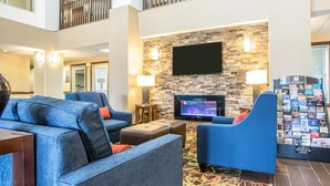 Un vestíbulo de hotel con pared de piedra, televisor de pantalla plana, asientos azules y un perchero para revistas.