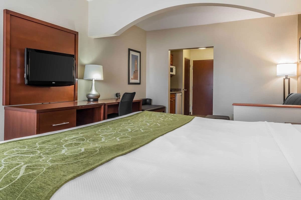 Une chambre d’hôtel équipée d’un lit, d’un bureau, d’une chaise, d’une télévision, d’une lampe et d’une porte donnant accès à une salle de bain.