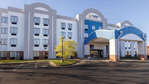 Un hotel Comfort Suites con diseño moderno, que presenta una entrada central con un arco azul, varias ventanas y un estacionamiento.