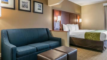 Una habitación de hotel con un sofá azul, un reposapiés marrón, una cama con una manta verde y tres cuadros en la pared.