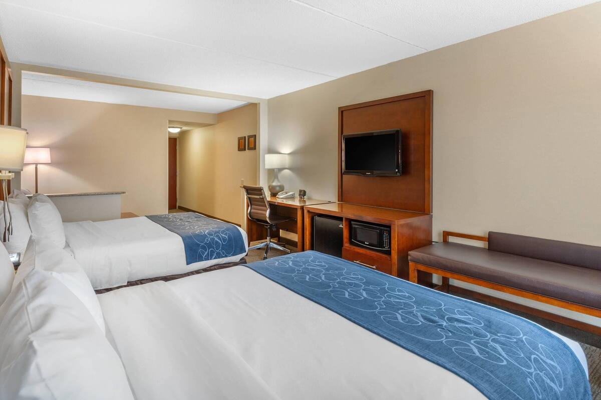 Ein Hotelzimmer mit zwei Betten, einem Schreibtisch mit Computer, einem Fernseher und einer Sitzecke.