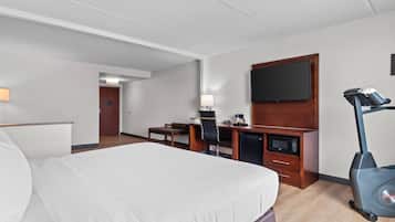 Habitación de hotel con cama, escritorio, silla, televisor, microondas y bicicleta estática.
