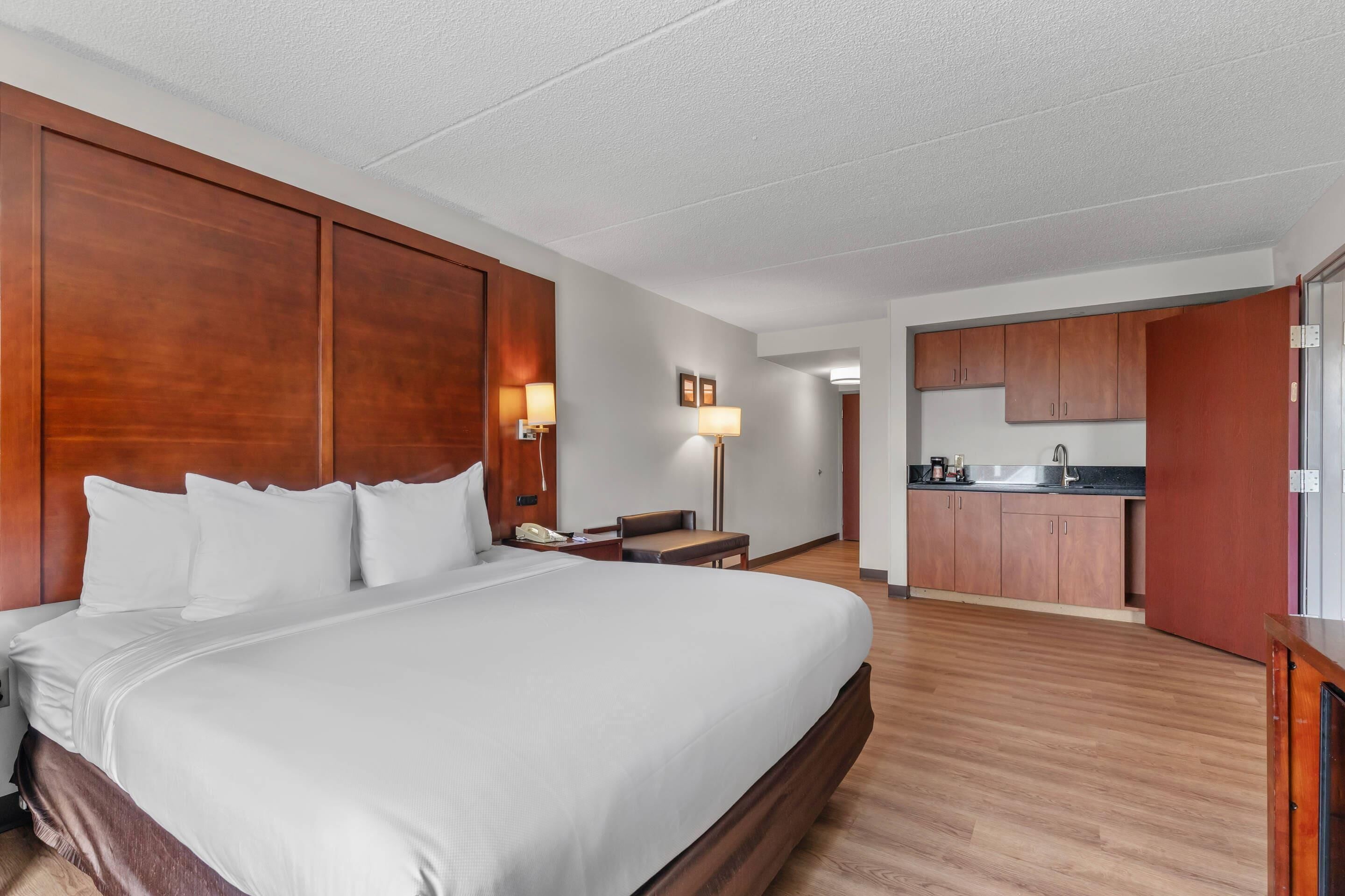 Une chambre d’hôtel avec un grand lit, un bureau, une chaise, une lampe et une kitchenette.