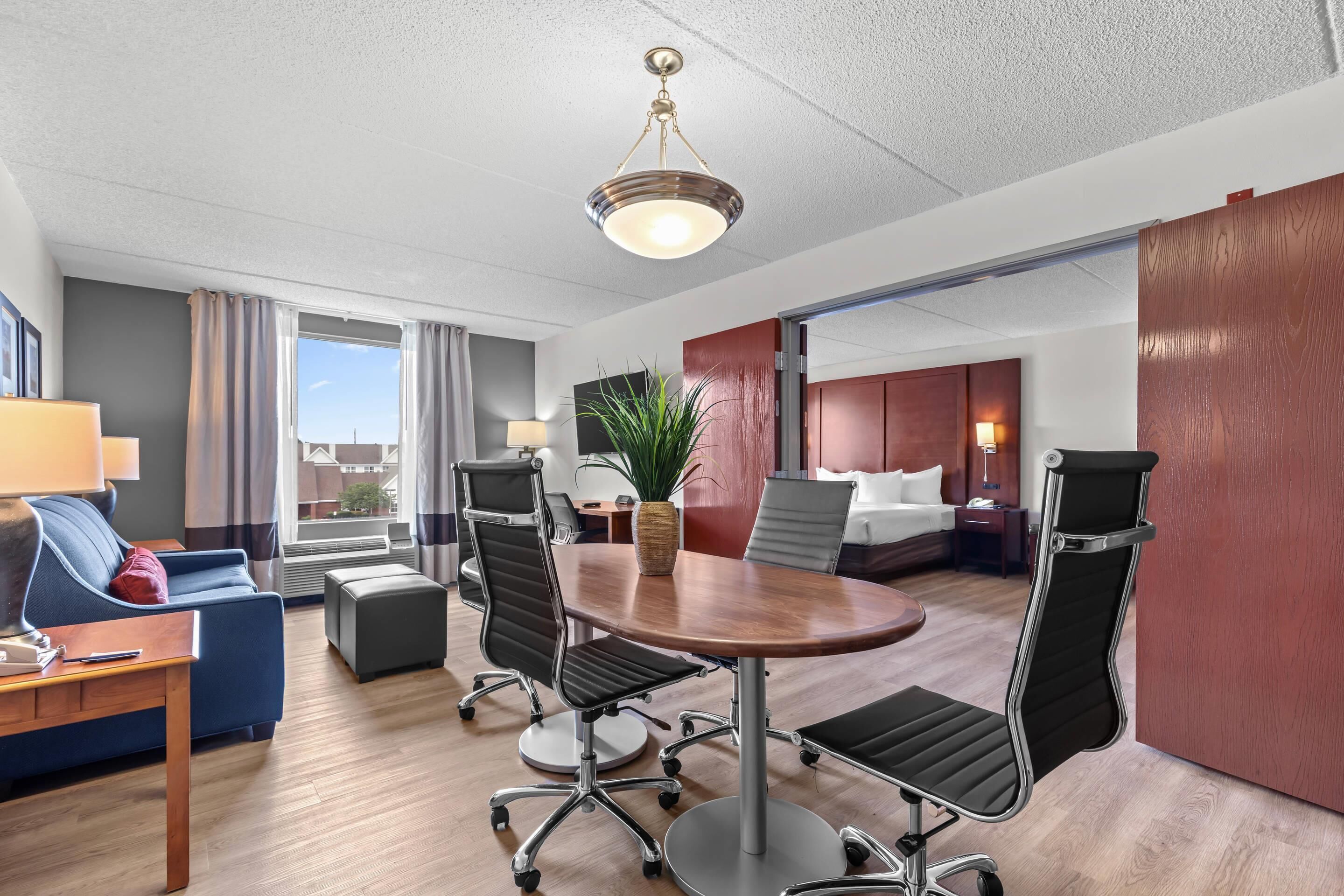 Une chambre d’hôtel équipée d’une table de conférence, de chaises, d’un canapé, d’un bureau, d’une lampe, d’une plante et d’un lit.