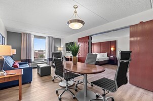 Habitación de hotel con una mesa de conferencias, sillas, un sofá, un escritorio, una lámpara, una planta y una cama.