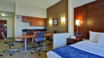 A hotel room with a bed, desk, chairs, and a kitchenette.