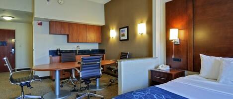 Habitación de hotel con cama, escritorio, sillas y kitchenette.