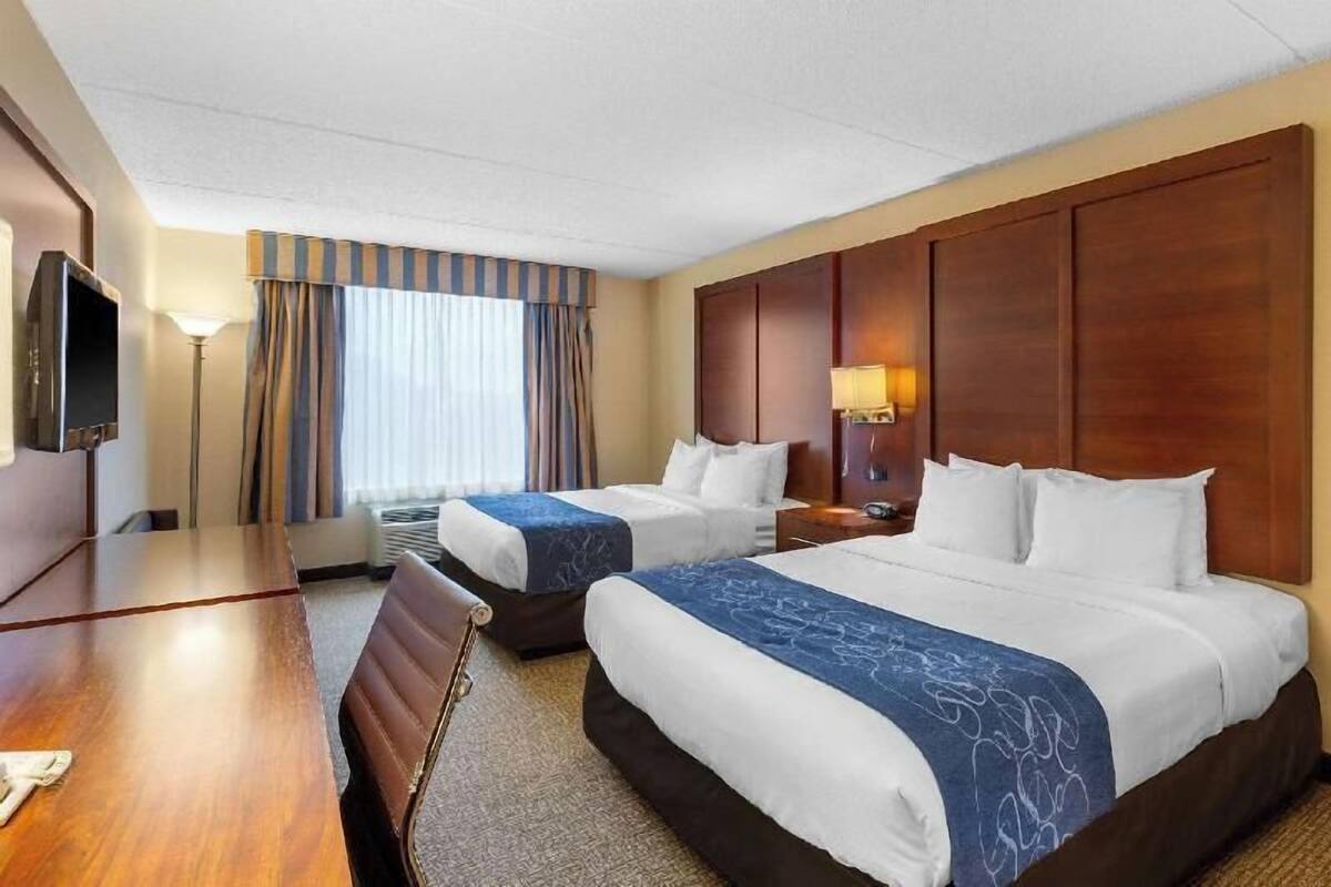 Ein Hotelzimmer mit zwei Betten, einem Schreibtisch, einem Fernseher und einem Fenster mit Vorhängen.