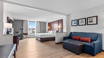A hotel room with a bed, a sofa, a desk, a chair, a treadmill, and a large window with a view.