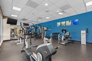 Un gimnasio con diverso equipo de ejercicio, dispensador de agua y decoración mural motivacional.