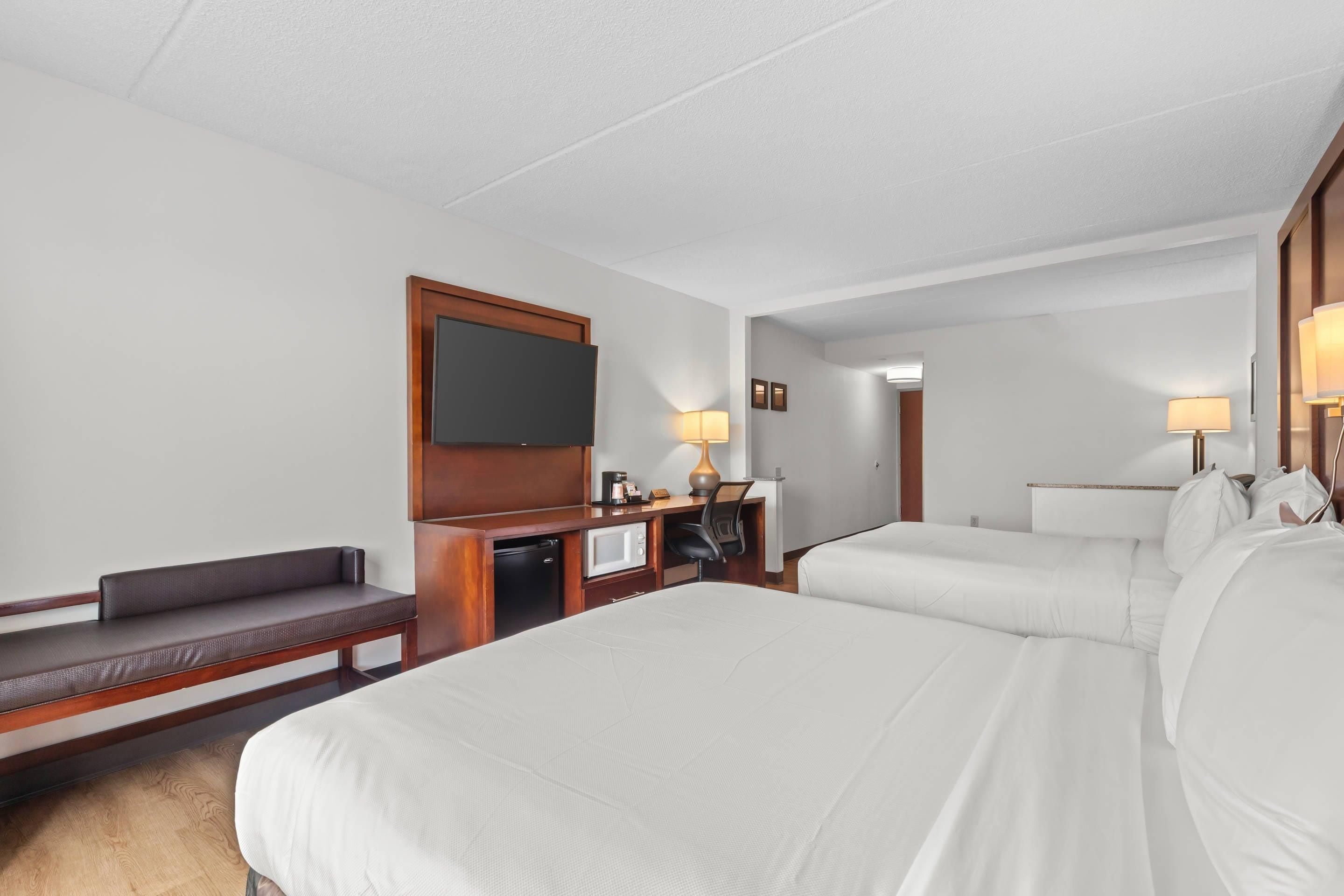 A hotel room with a large bed, a desk with a computer, a television, and two bedside lamps.