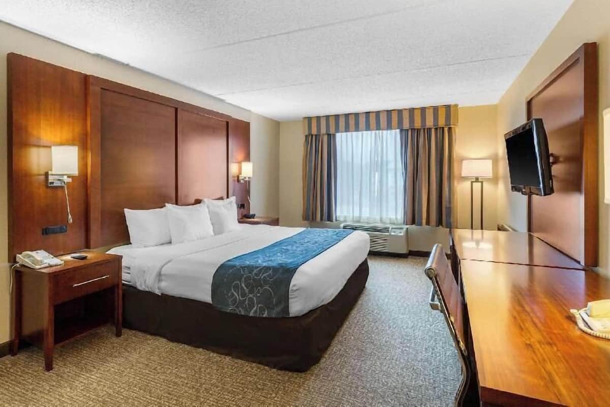 Ein Hotelzimmer mit einem großen Bett, einem Schreibtisch, einem Fernseher und einem Fenster mit Vorhängen.