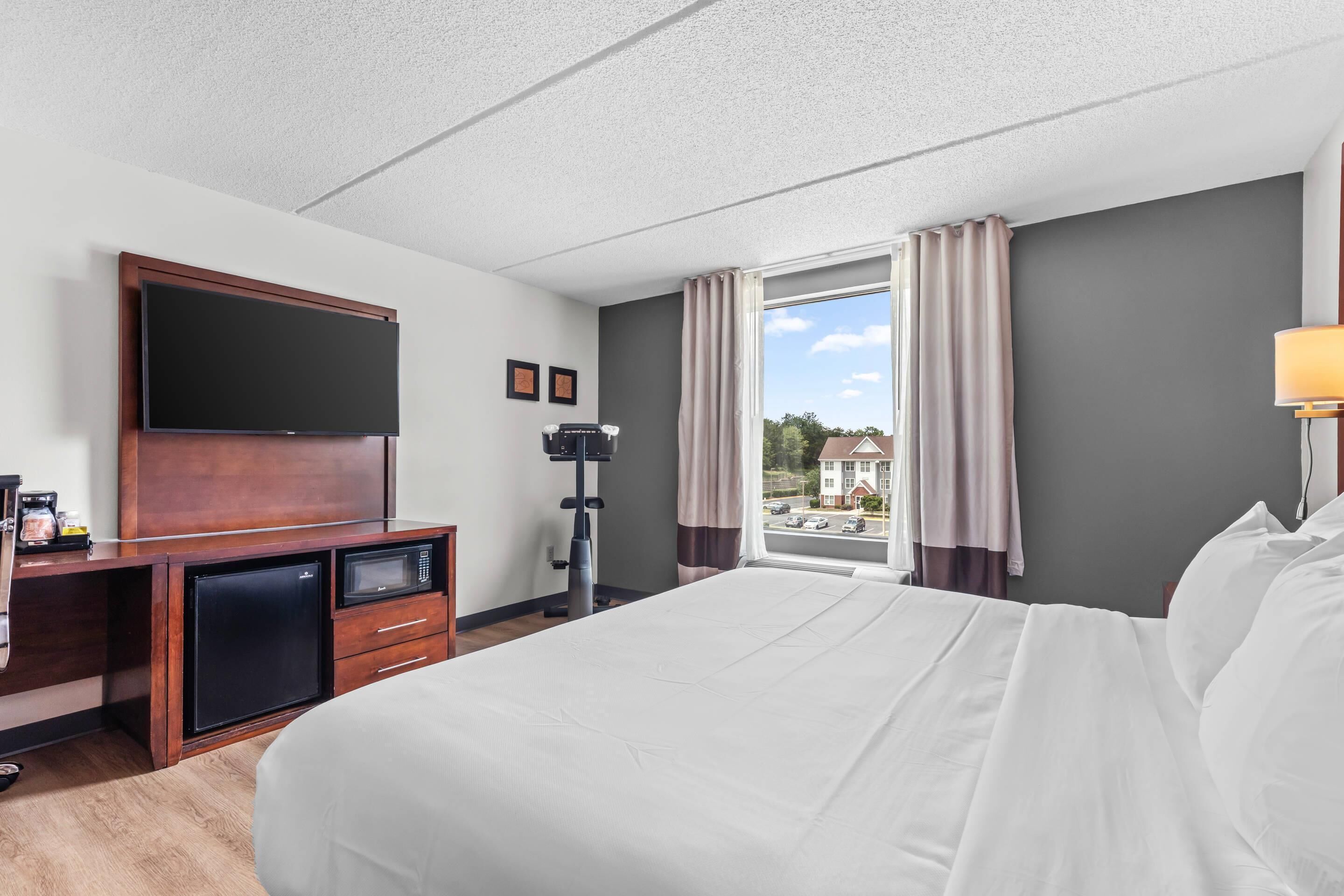 A hotel room with a bed, a desk with a flat-screen TV, a microwave, and a coffee machine.