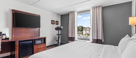 A hotel room with a bed, a desk with a flat-screen TV, a microwave, and a coffee machine.