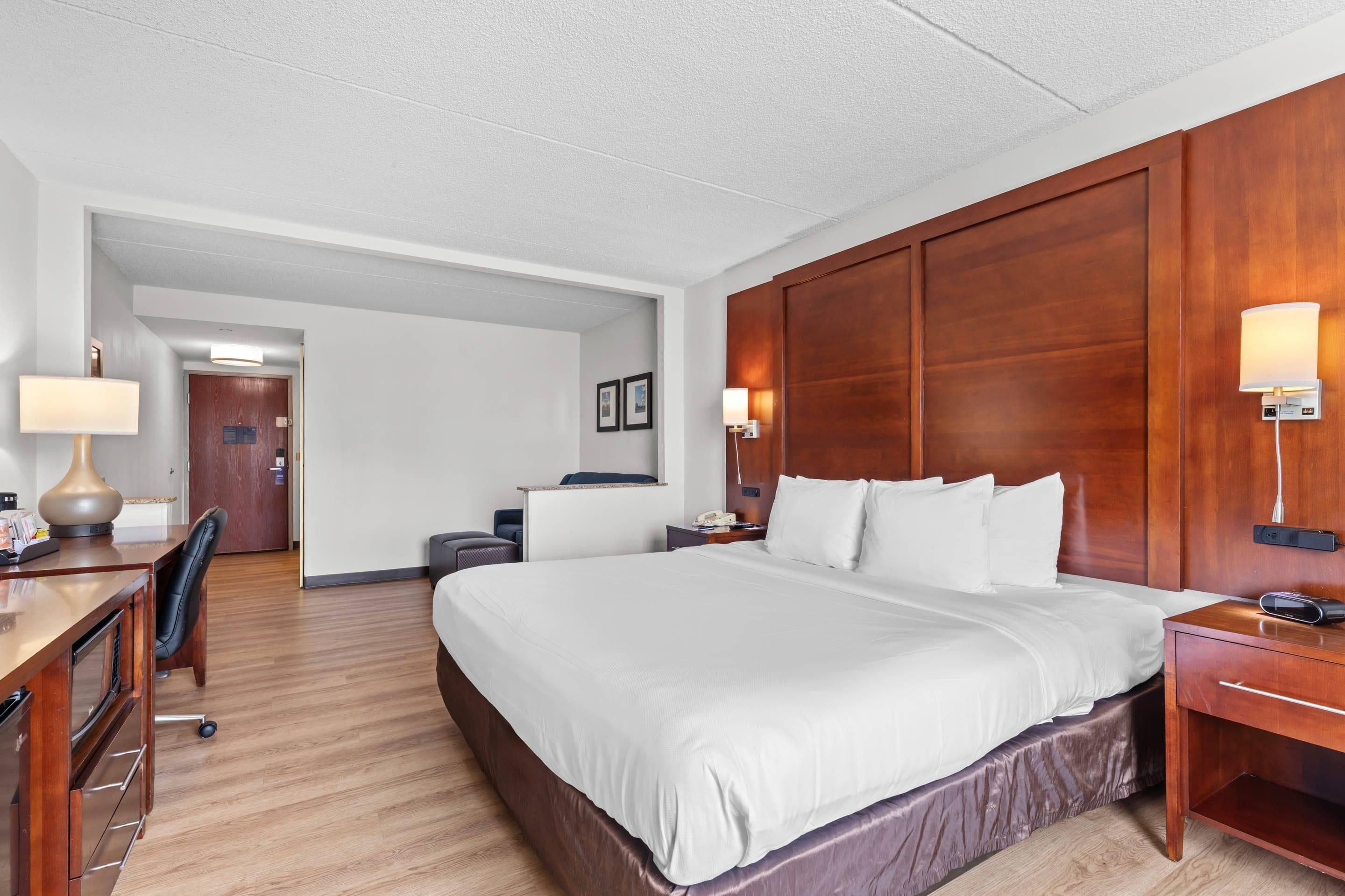 Une chambre d’hôtel avec un grand lit, une tête de lit en bois, des tables de chevet avec des lampes, un bureau avec une chaise et une lampe de bureau.