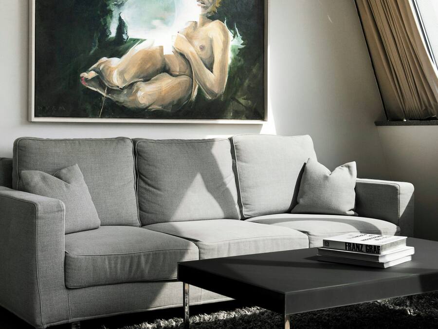 A modern living room with a grey sofa, a black coffee table, and a framed painting above the sofa.