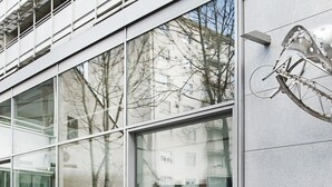 Um edifício moderno com grandes janelas, uma escultura de bicicleta e uma mesa amarela com design em estrutura de arame.