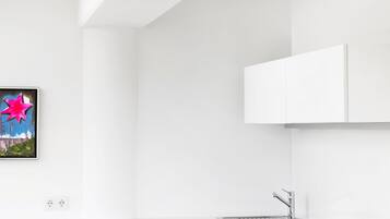 Una cocina moderna con armarios blancos, una silla de comedor negra y un cuadro de colores en la pared.