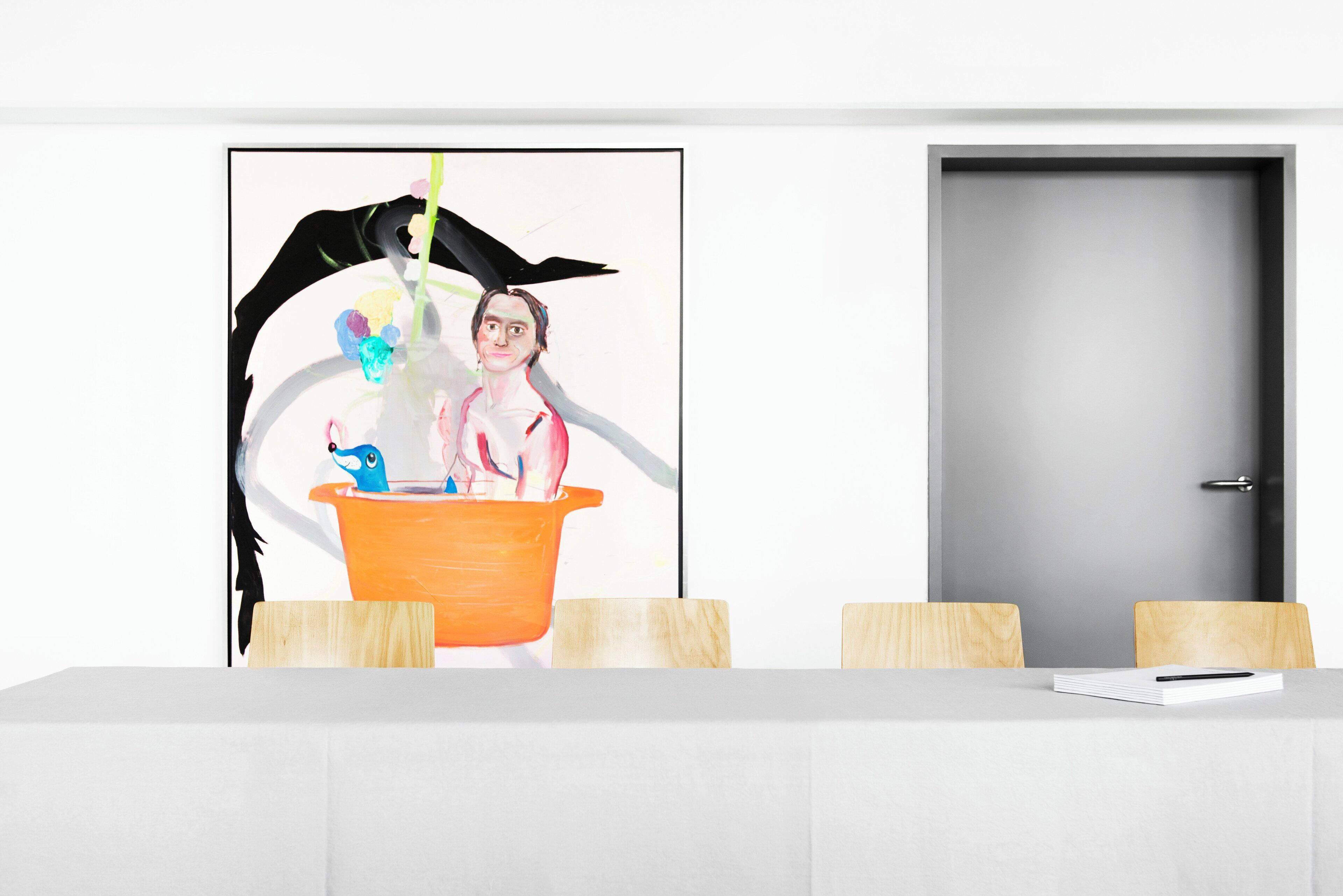 A room with a white table, two wooden chairs, a door, and a colorful abstract painting on the wall.