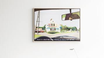 Ein moderner Arbeitsraum mit einem weißen Schreibtisch, einem blauen Hocker und einem gerahmten Bild von einer Autohaus-Werbung an der Wand.