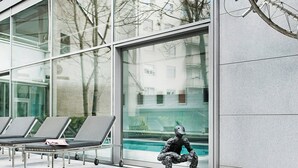 Um edifício moderno com amplas janelas, área de estar externa e uma escultura.