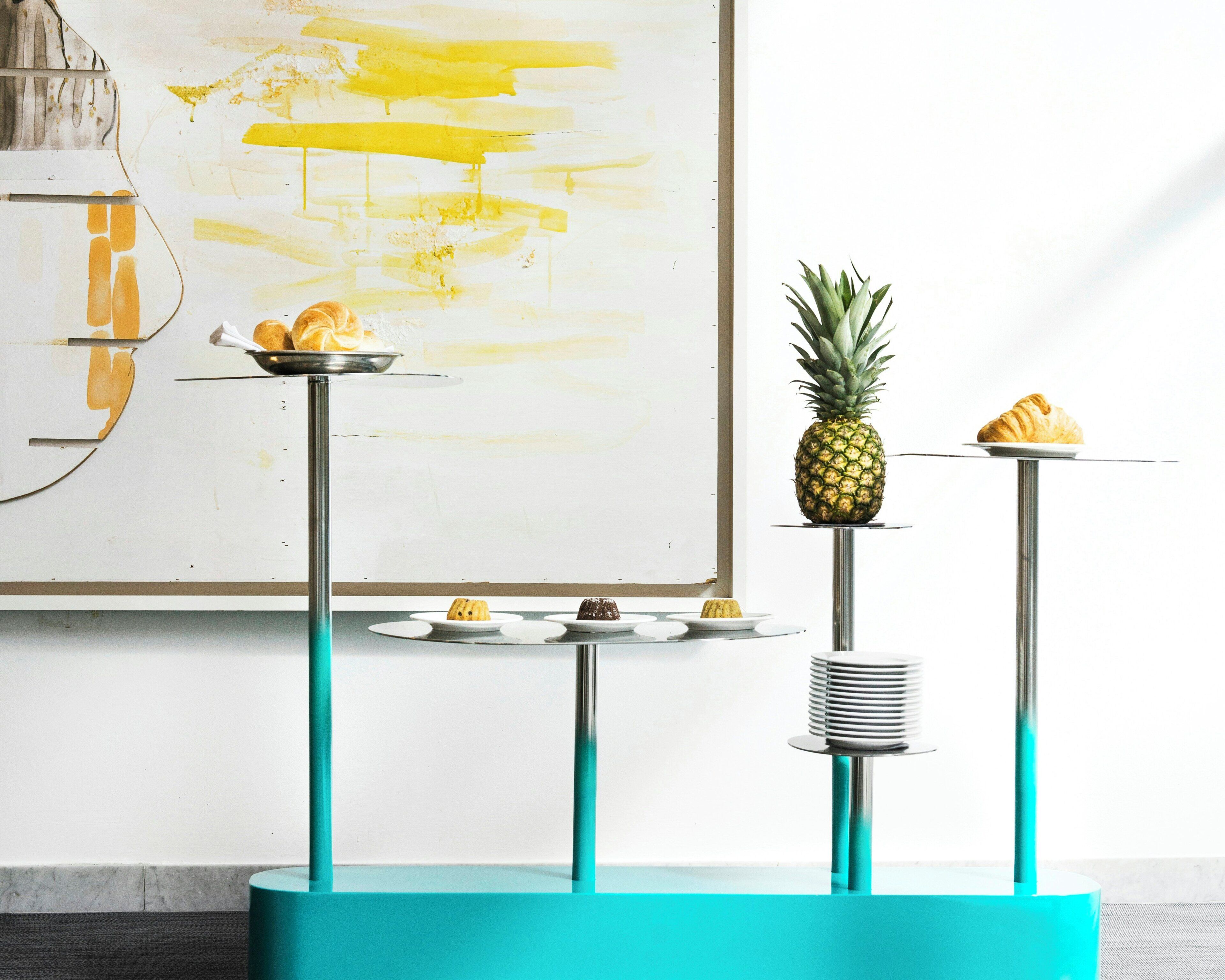 A dessert display with various pastries and a pineapple on a teal stand.