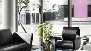 Um espaço de escritório moderno com uma mesa de centro de vidro, cadeiras pretas e brancas e um vaso com flores.