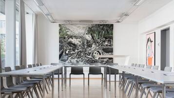 A conference room with a long table and chairs, a large abstract painting on the wall, and a window providing natural light.