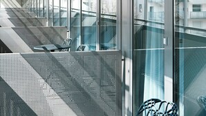 Um edifício moderno com fachada de vidro, grades de metal e escadaria que leva a um andar superior.