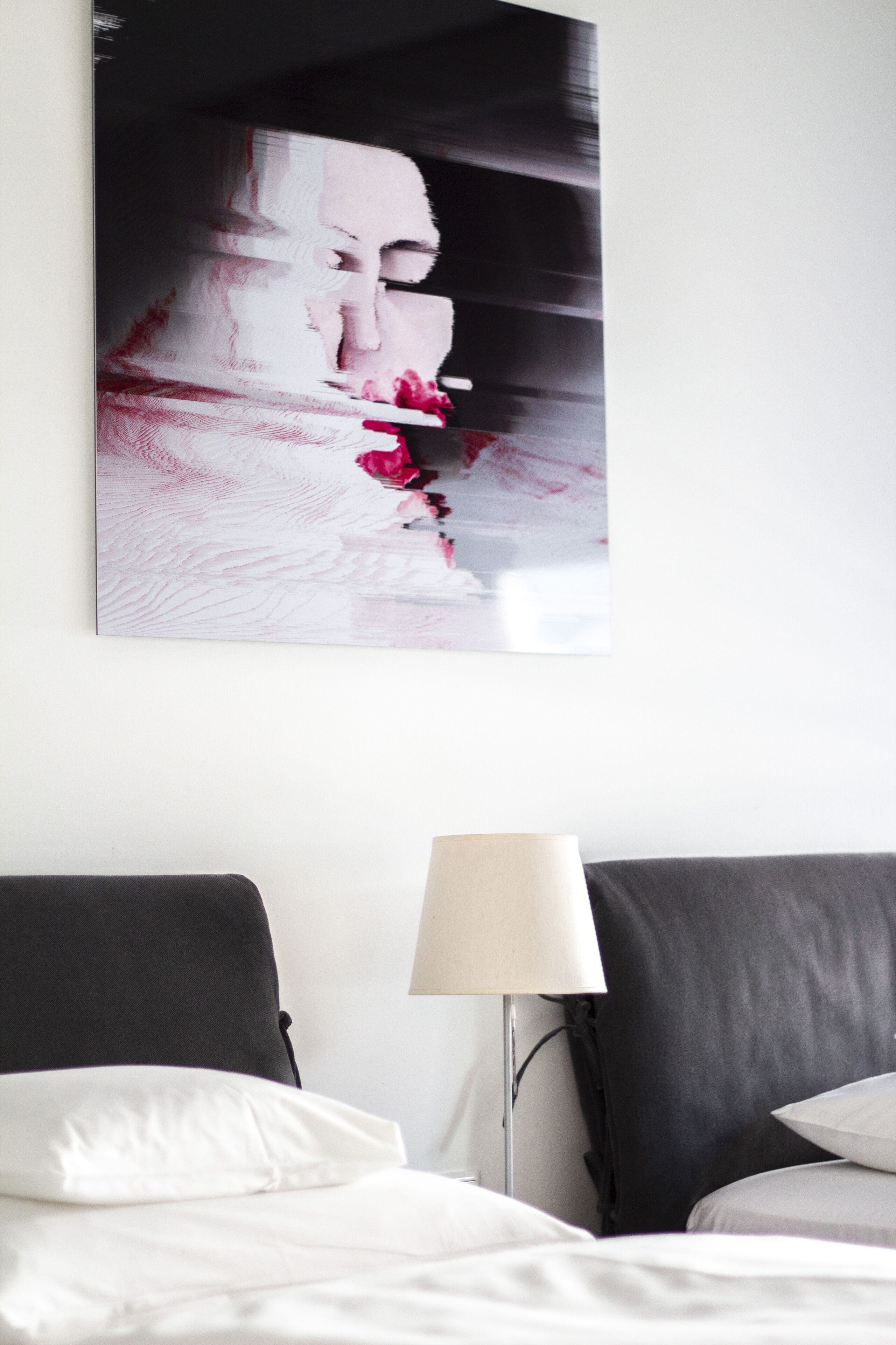 A hotel room with a bed, a nightstand, and a wall-mounted artwork.