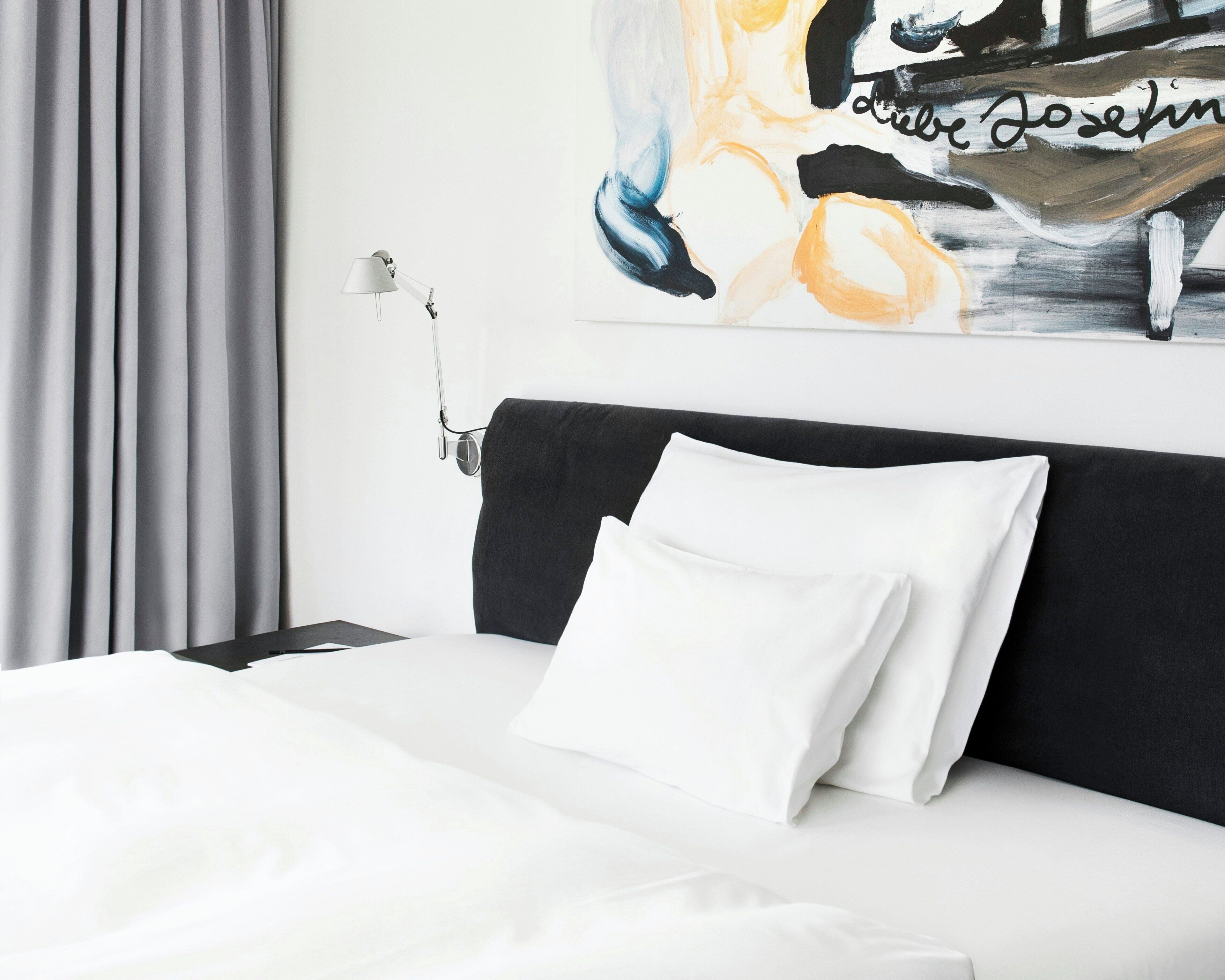 A hotel room with a bed, a nightstand, a lamp, and a painting on the wall.