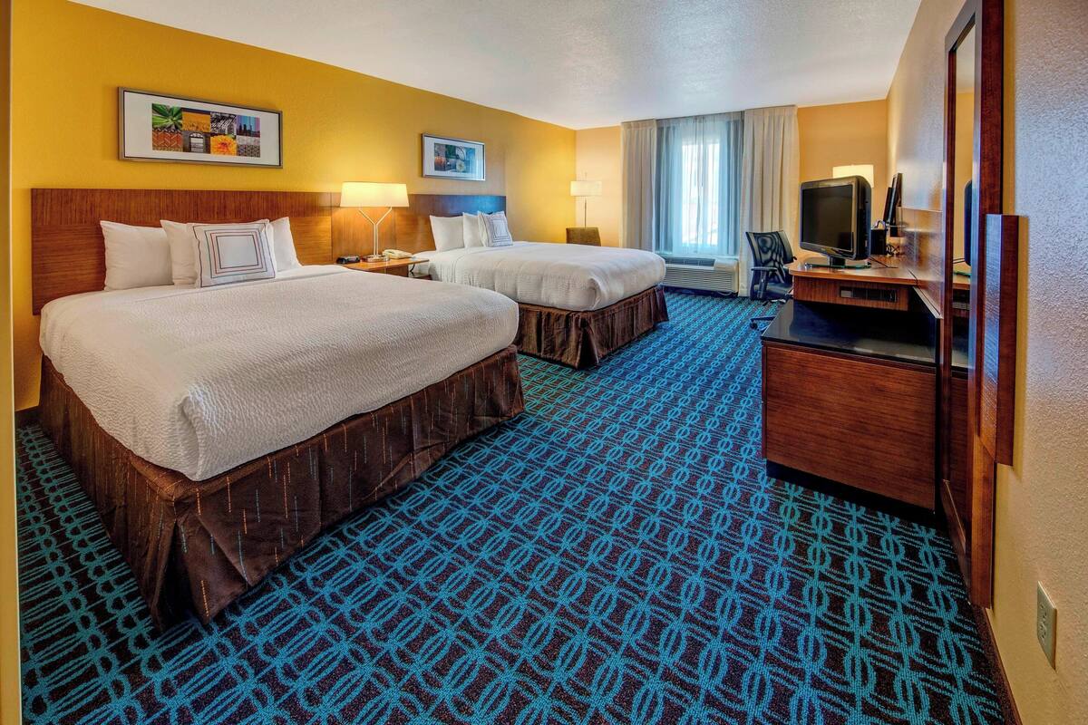 A hotel room with two beds, a TV, and a desk.