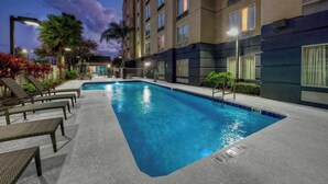 A swimming pool with lounge chairs and a building with multiple windows. - Fairfield Inn & Suites by Marriott Near Universal Orlando (Orlando)